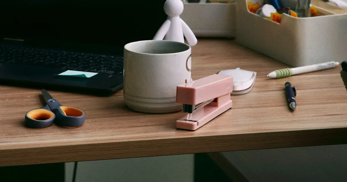 Escritorio de trabajo con una taza, una engrapadora, tijeras y una laptop, como imagen del regreso al trabajo después del tratamiento